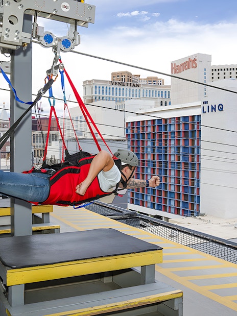 Person on Fly LINQ Zipline above Las Vegas with city buildings in background.