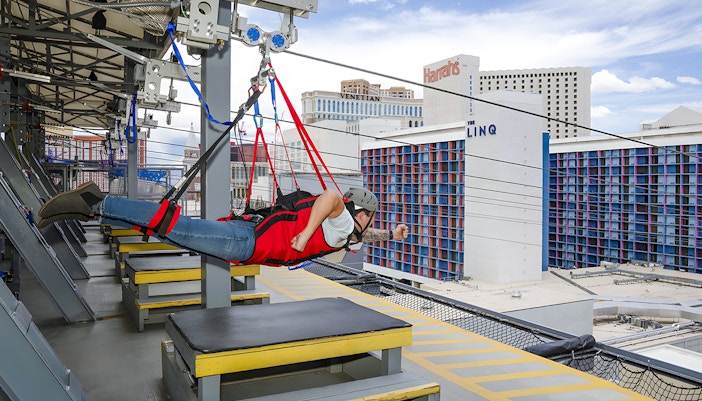 Person on Fly LINQ Zipline above Las Vegas with city buildings in background.