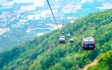 Cable cars ascending Black Virgin Mountain, Tay Ninh, with views of lush greenery and distant fields.