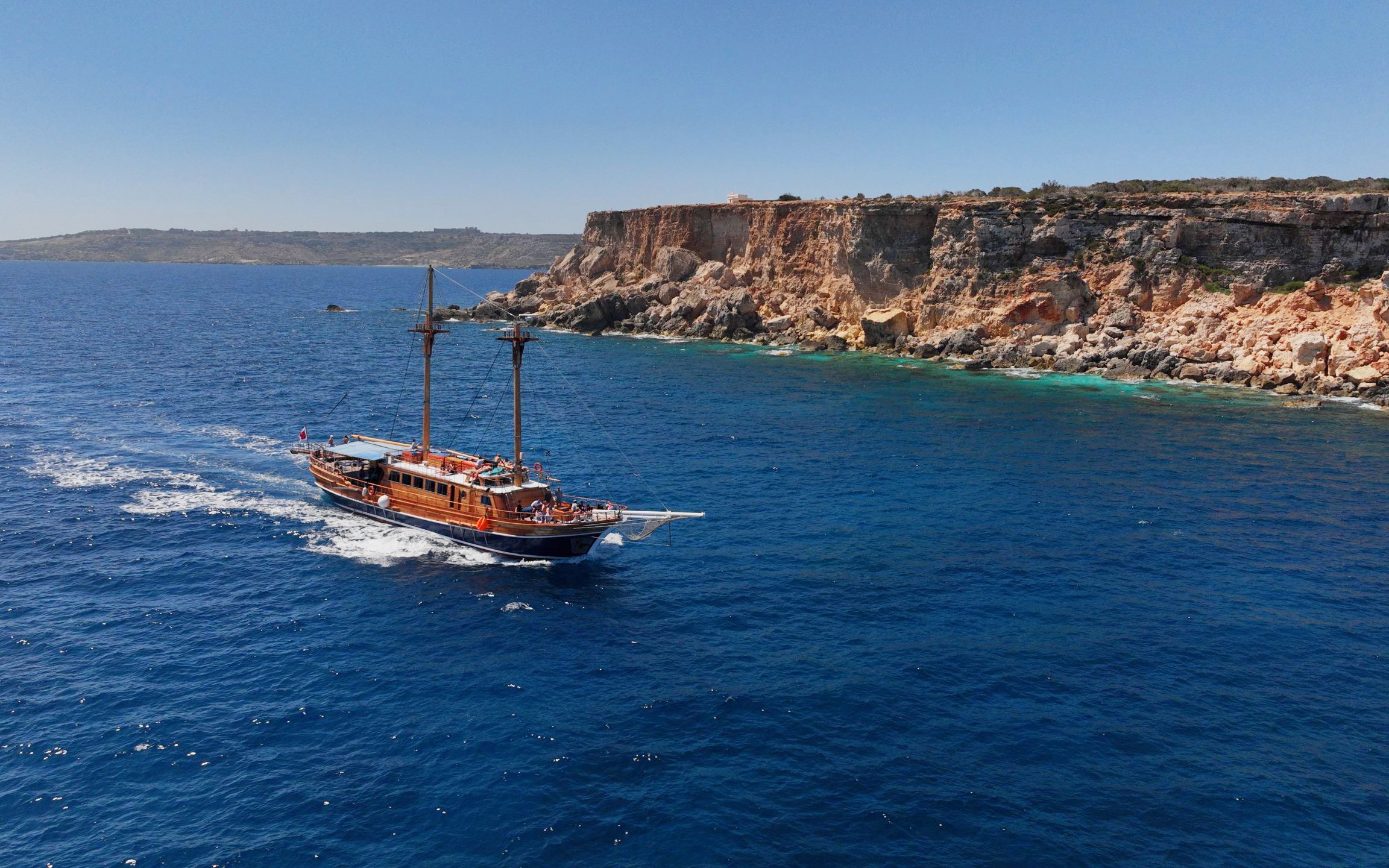 Cruise ship sailing near rocky cliffs on the Fernandes Gozo & Comino all-inclusive tour.