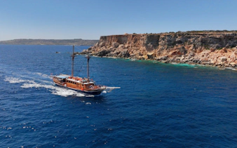 Cruise ship sailing near rocky cliffs on the Fernandes Gozo & Comino all-inclusive tour.