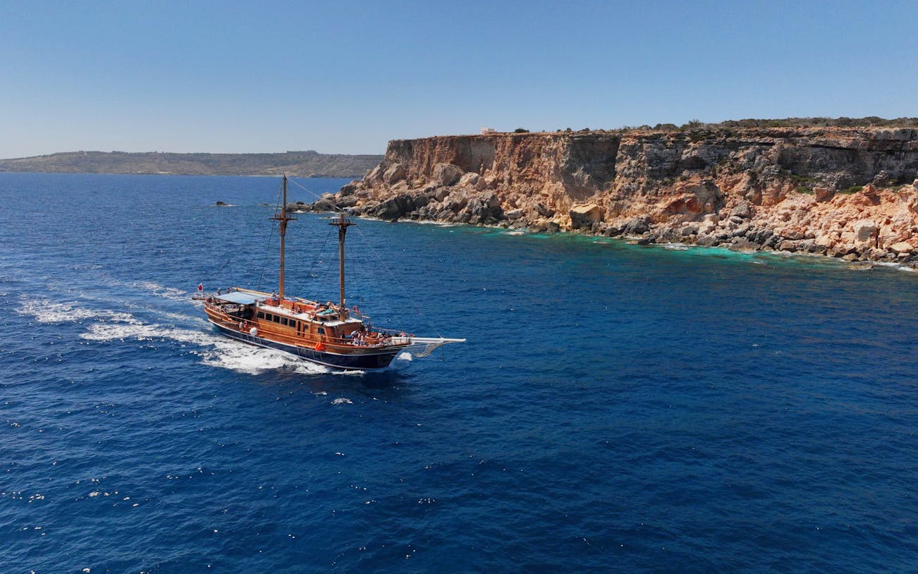Cruise ship sailing near rocky cliffs on the Fernandes Gozo & Comino all-inclusive tour.