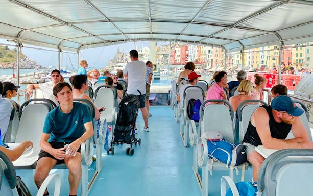Tourists on a ferry during a guided tour of Cinque Terre from La Spezia, with colorful buildings in view.