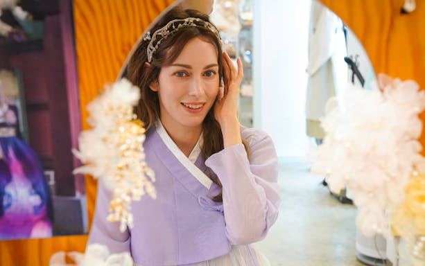 Hanbok rental experience with a woman in traditional Korean attire adjusting her hair in a mirror.