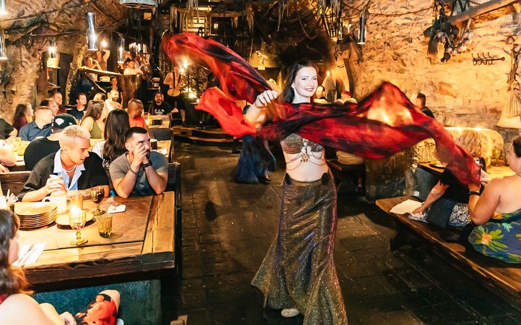 Belly dancer performing at a medieval-themed dinner with guests seated at wooden tables.