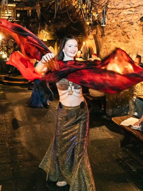 Belly dancer performing at a medieval-themed dinner with guests seated at wooden tables.