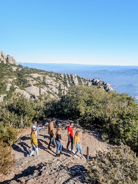 Tourists hiking with guide on trail to Montserrat Monastery, Spain, with mountain views.
