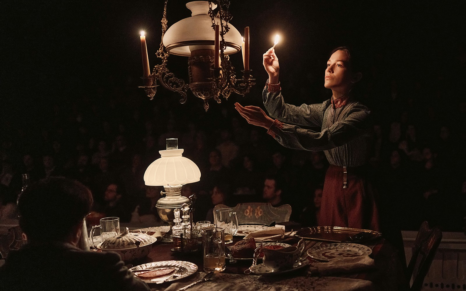 Theater scene from "An Enemy of the People" with a woman lighting a chandelier.