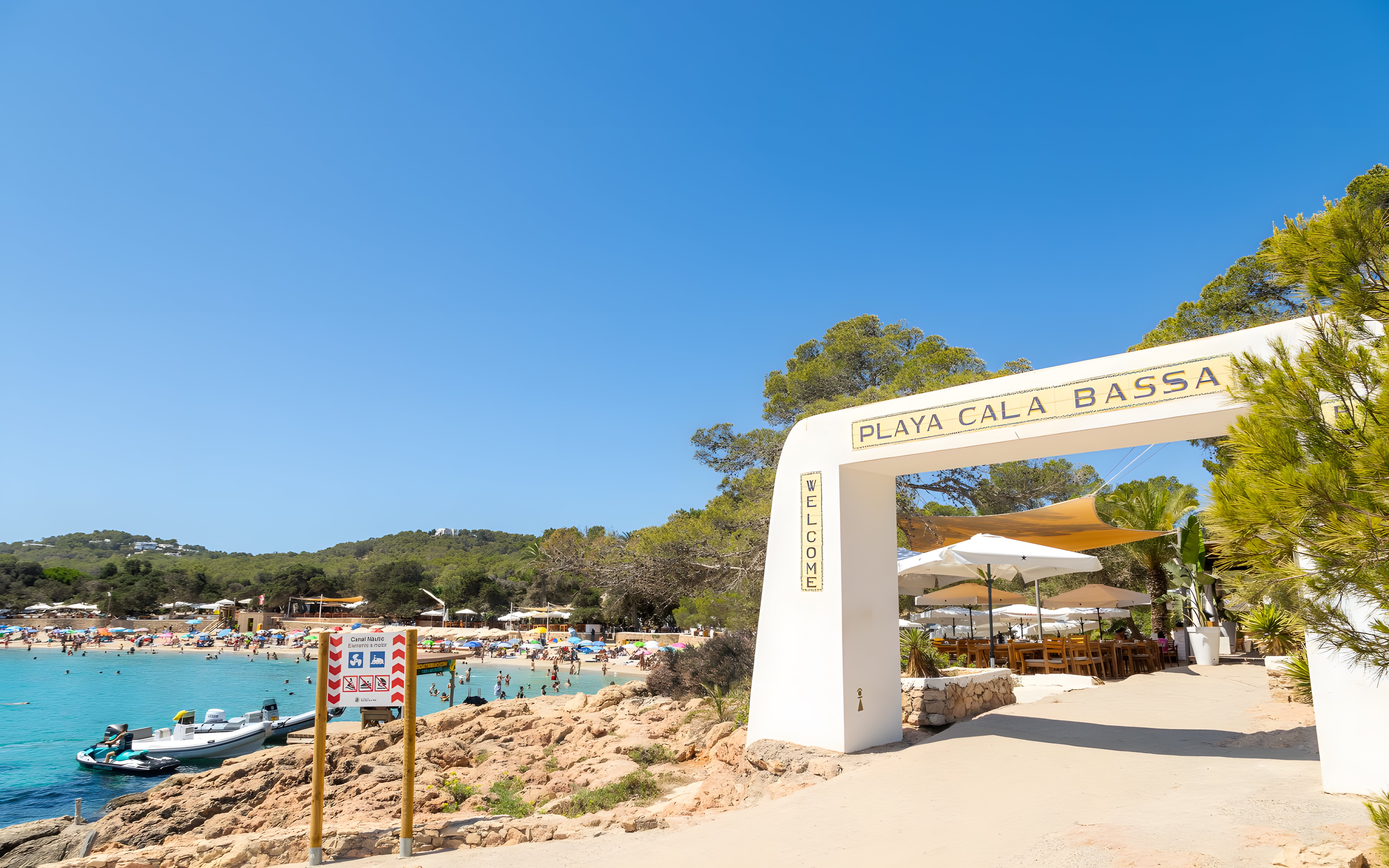 Entrance to Cala Bassa beach with view of sandy shore and clear water in Ibiza, Spain.