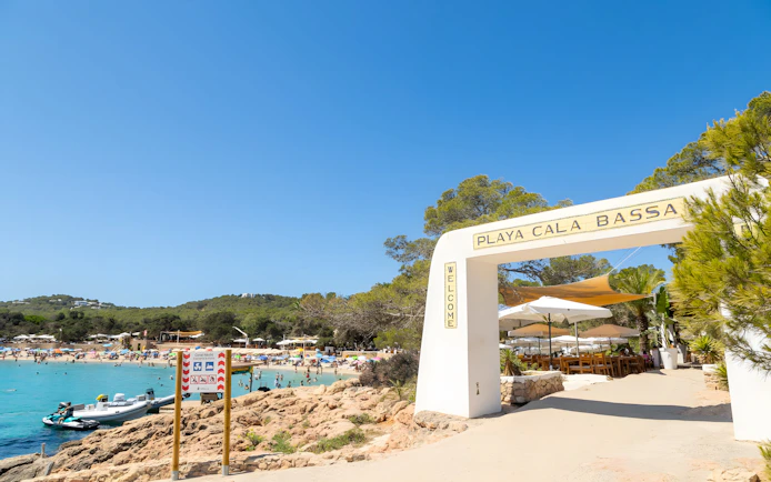 Entrance to Cala Bassa beach with view of sandy shore and clear water in Ibiza, Spain.