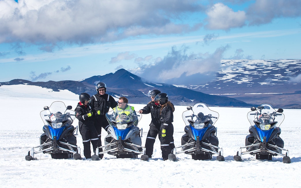Snowmobile riders on Langjokull Glacier with snowy mountains in the background.