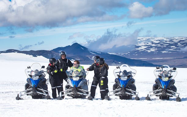 Snowmobile riders on Langjokull Glacier with snowy mountains in the background.