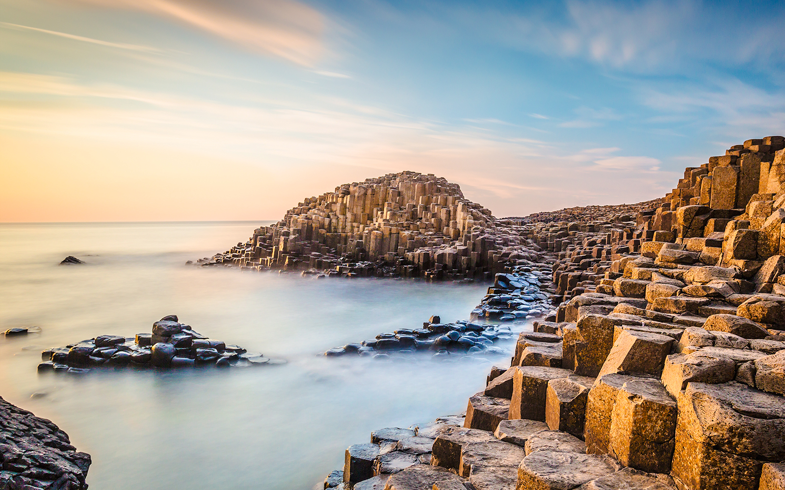 Giant's Causeway basalt columns at evening with calm sea and sunset sky.