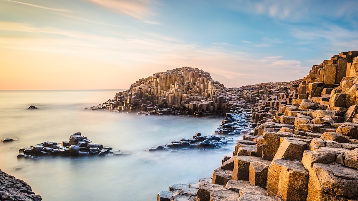 Giant's Causeway basalt columns at evening with calm sea and sunset sky.