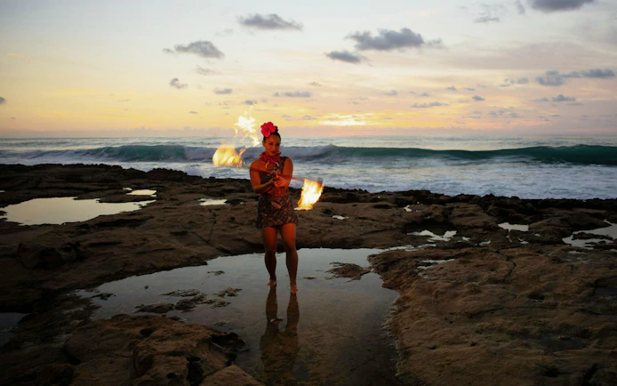Fire dancer performing at sunset on a rocky beach during Kaula-Luau.