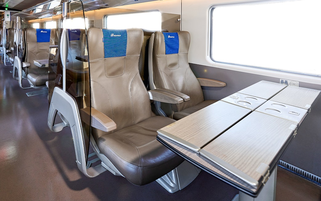Trenitalia business class seats with foldable tables and leather upholstery.