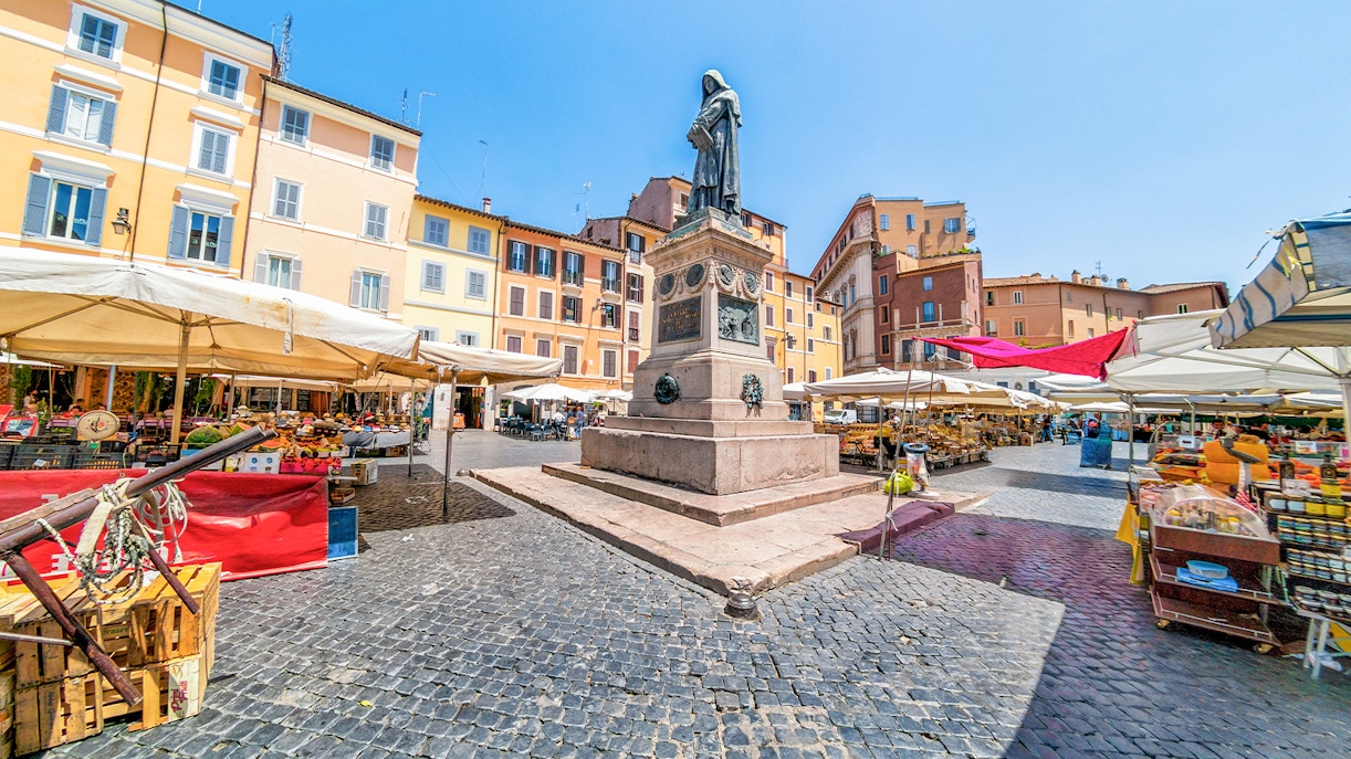 Giordano Bruno statue at Campo de’ Fiori market with gourmet food stalls in Rome.