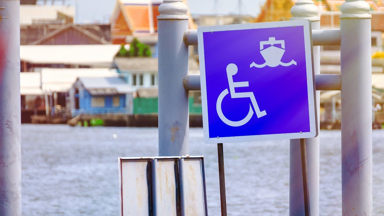 Wheelchair access sign at a pier with boats in the background.