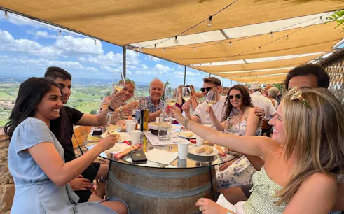 Group enjoying wine tasting at a Tuscan winery with scenic vineyard views.