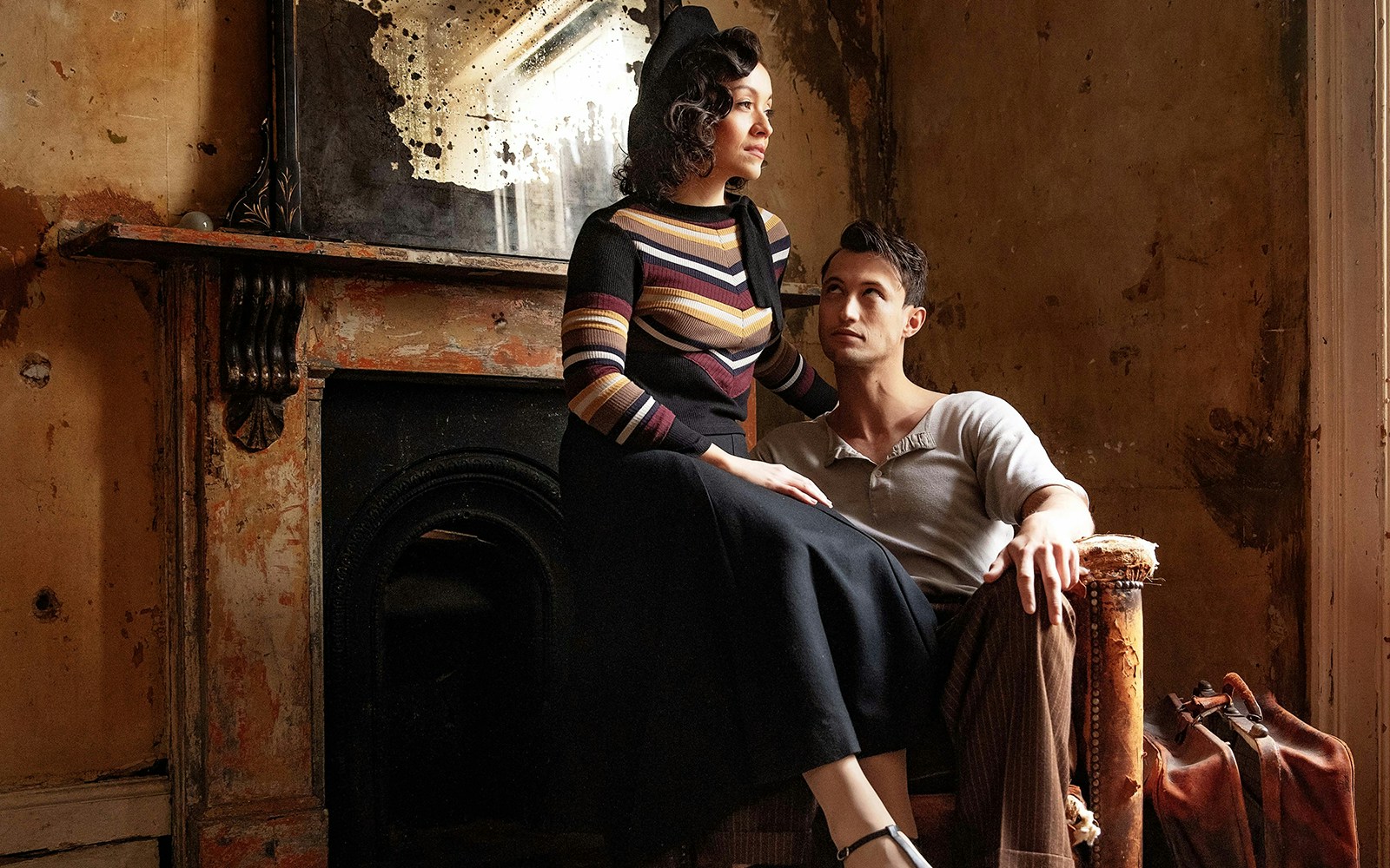Couple in vintage attire sitting in a rustic room, evoking Bonnie & Clyde era.