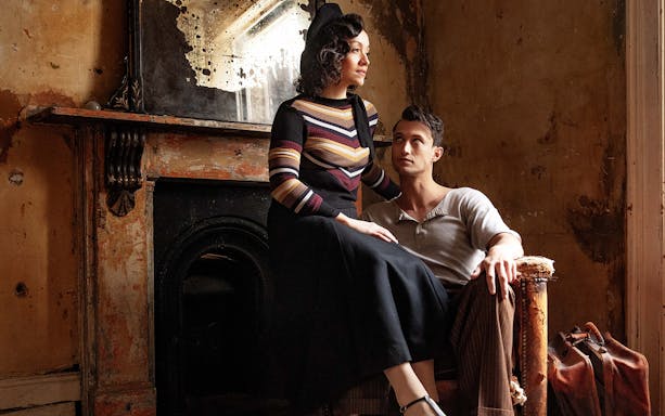 Couple in vintage attire sitting in a rustic room, evoking Bonnie & Clyde era.