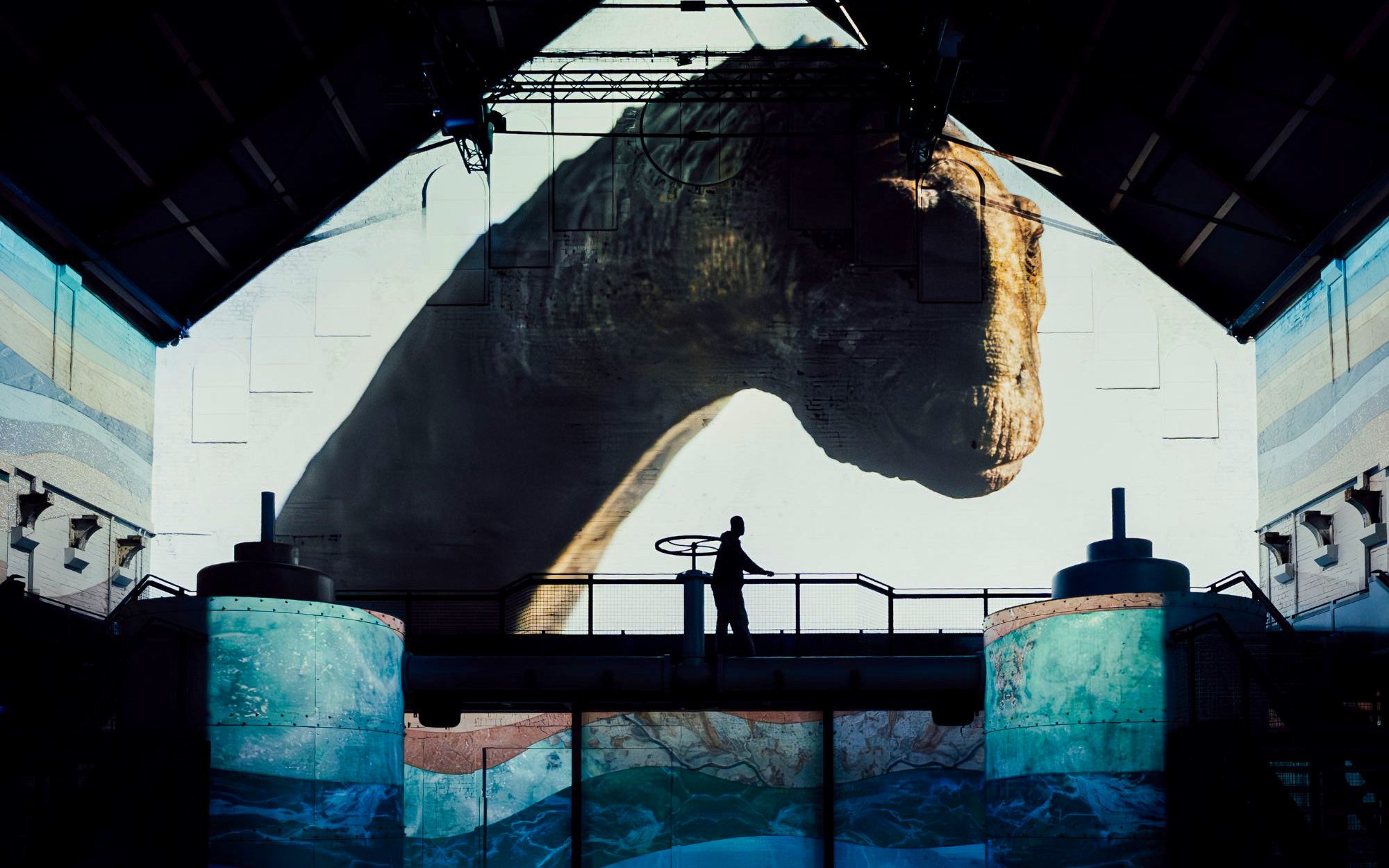 Dinosaur projection at Fabrique des Lumières exhibition with silhouetted visitor.