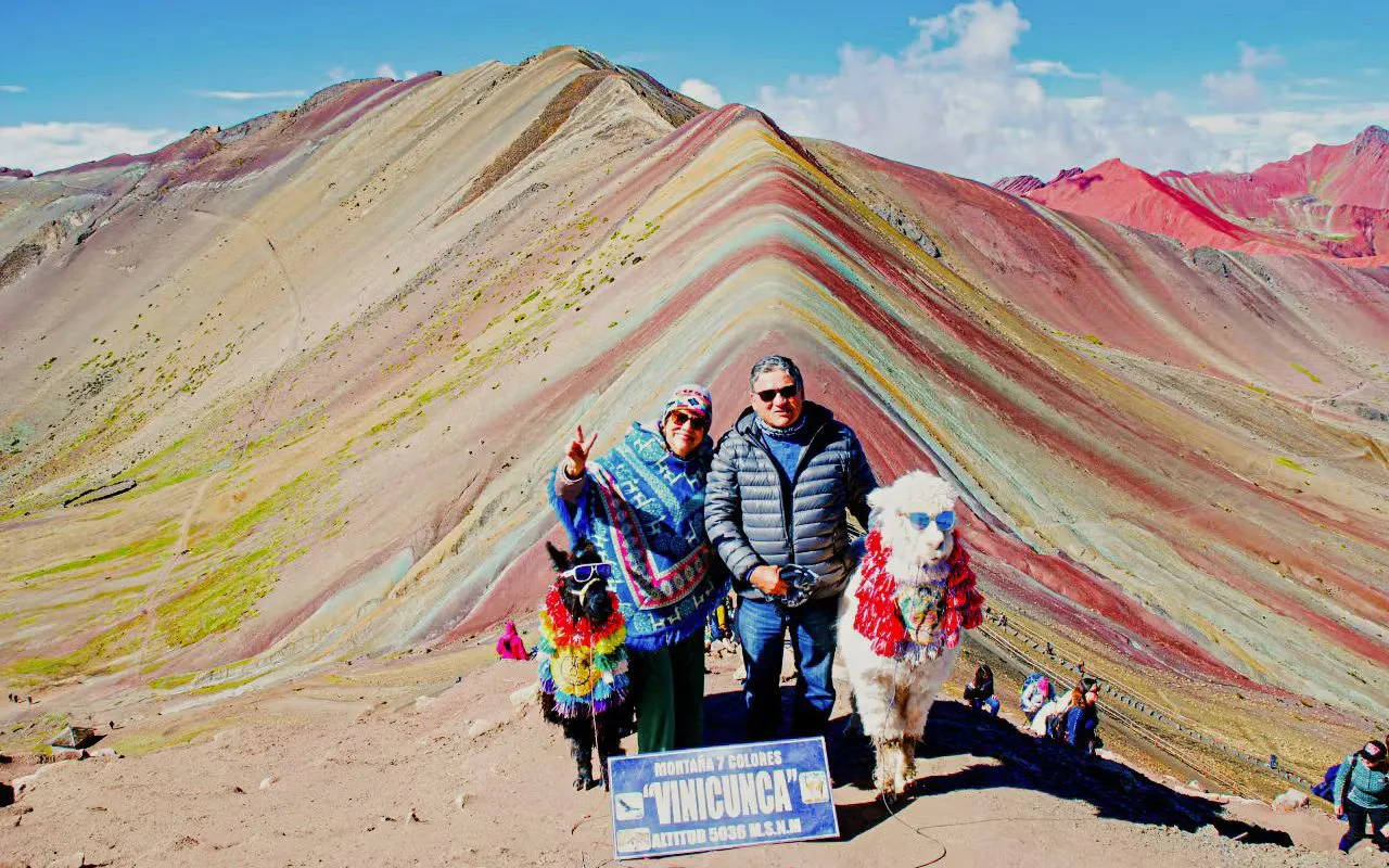 Visitors at Rainbow Mountain, Peru, with alpacas and colorful landscape in the background.