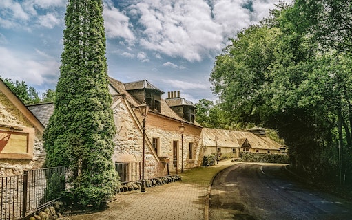 Historic distillery building surrounded by trees on the Ultimate Whisky Experience from Edinburgh.