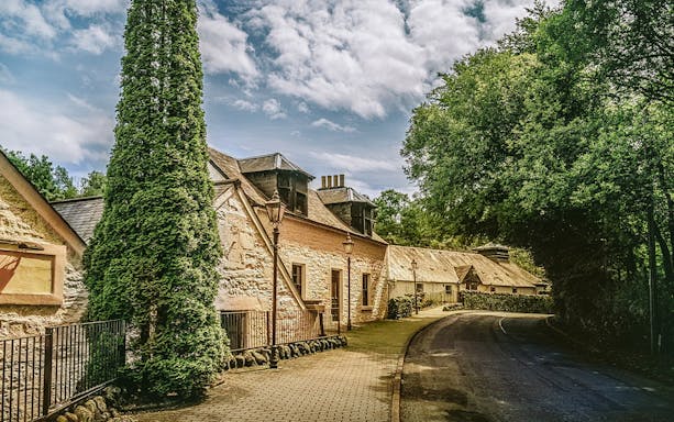 Historic distillery building surrounded by trees on the Ultimate Whisky Experience from Edinburgh.