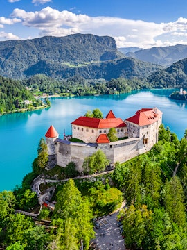 Aerial view of Bled Castle overlooking Lake Bled, Slovenia, surrounded by lush greenery.