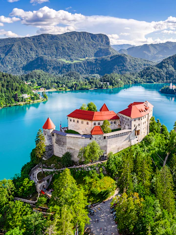 Aerial view of Bled Castle overlooking Lake Bled, Slovenia, surrounded by lush greenery.