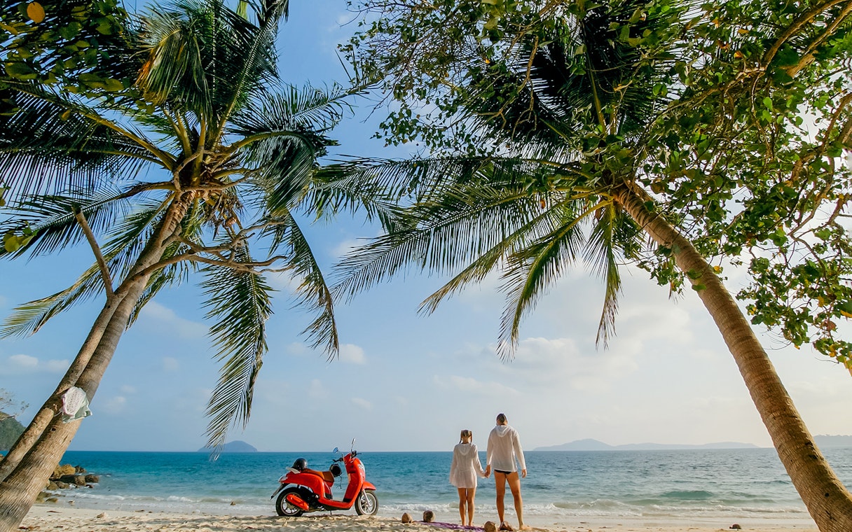 Couple on Langkawi beach with red motorbike under palm trees.