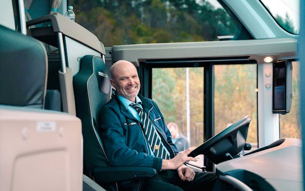 Bus driver smiling while seated in a coach during a transfer.