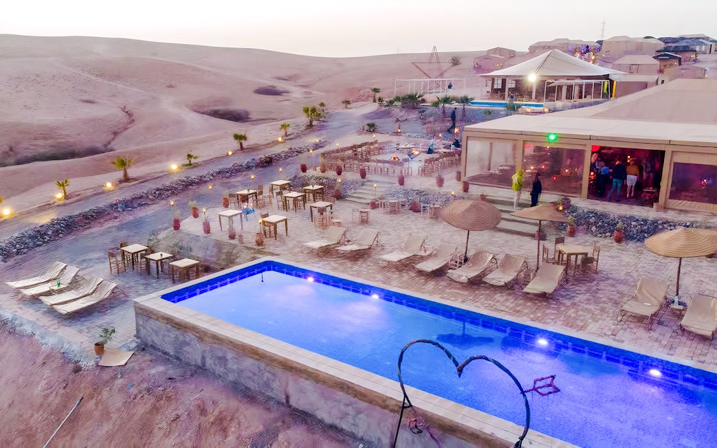 Marrakech Agafay desert camp with pool and seating area at sunset.