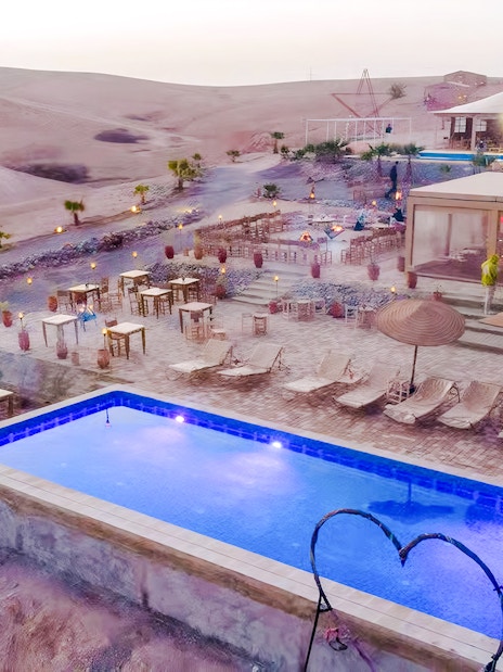 Marrakech Agafay desert camp with pool and seating area at sunset.