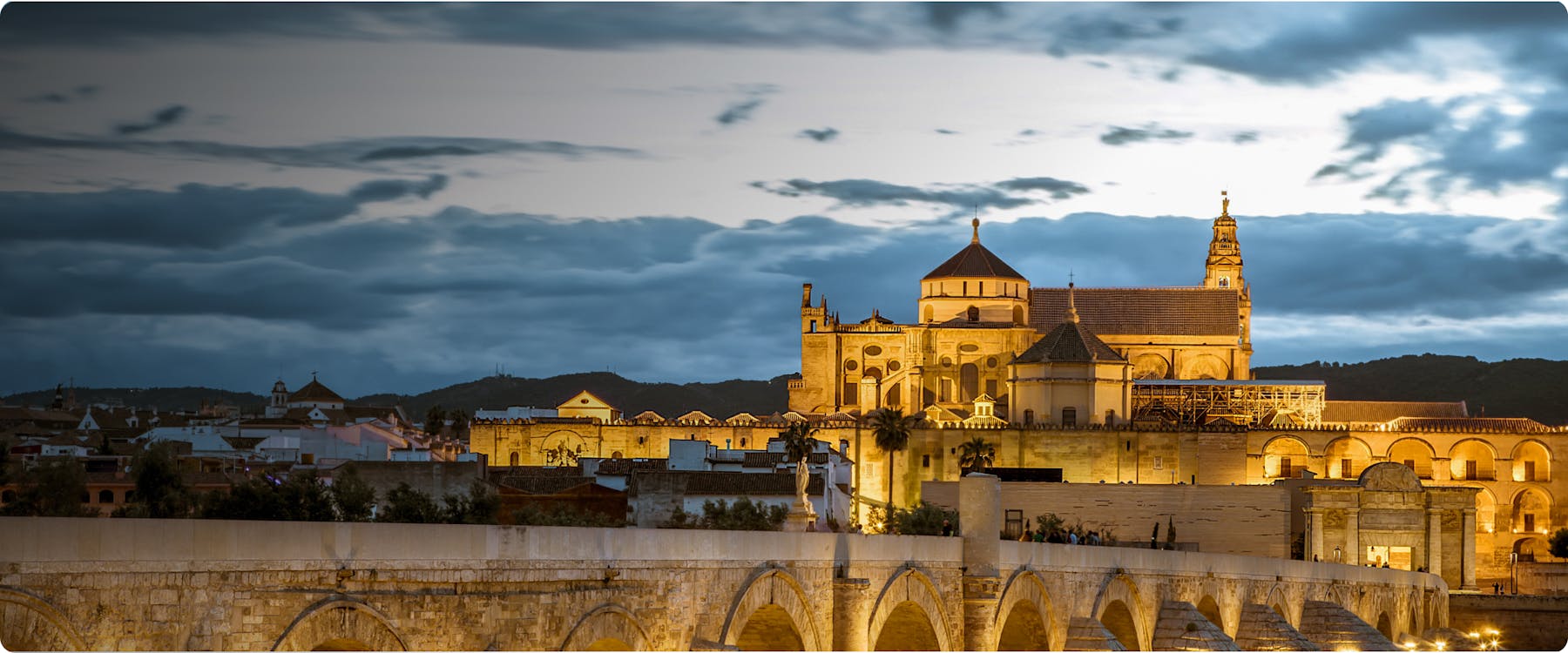 Mosque-Cathedral of Córdoba illuminated at dusk with Roman Bridge in foreground.