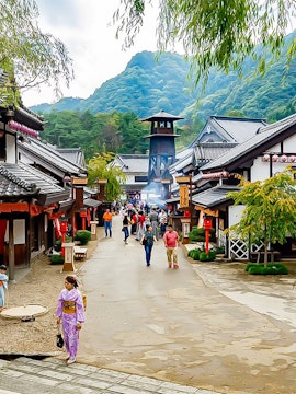 Visitors walking through Edo Wonderland, Japan, with traditional buildings and mountainous backdrop.