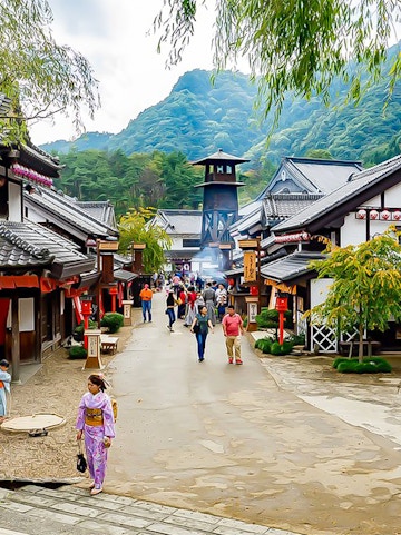 Visitors walking through Edo Wonderland, Japan, with traditional buildings and mountainous backdrop.