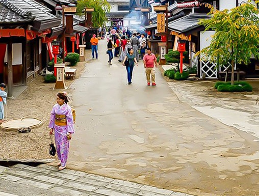 Visitors walking through Edo Wonderland, Japan, with traditional buildings and mountainous backdrop.