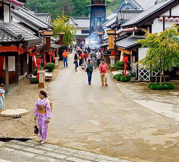 Visitors walking through Edo Wonderland, Japan, with traditional buildings and mountainous backdrop.