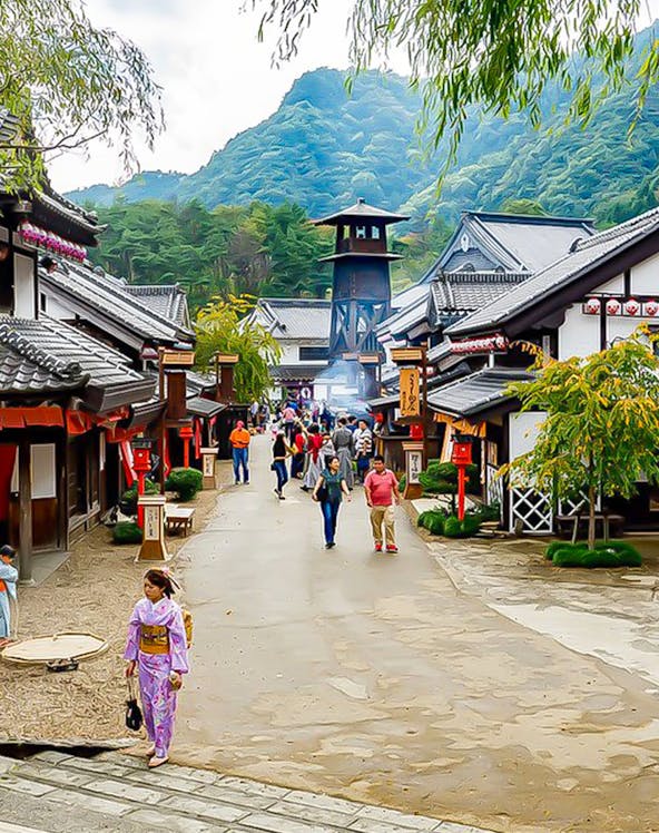 Visitors walking through Edo Wonderland, Japan, with traditional buildings and mountainous backdrop.