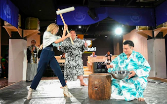 Person lifting wooden mallet for mochitsuki, traditional Japanese mochi pounding, with mortar and rice.