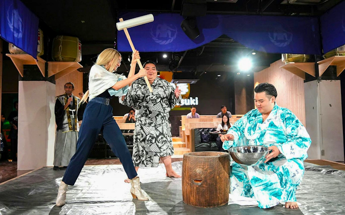 Person lifting wooden mallet for mochitsuki, traditional Japanese mochi pounding, with mortar and rice.