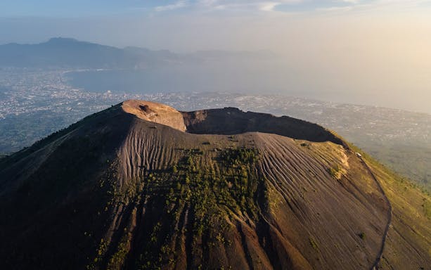 Aerial view of Mount Vesuvius crater with Naples coastline in the background.