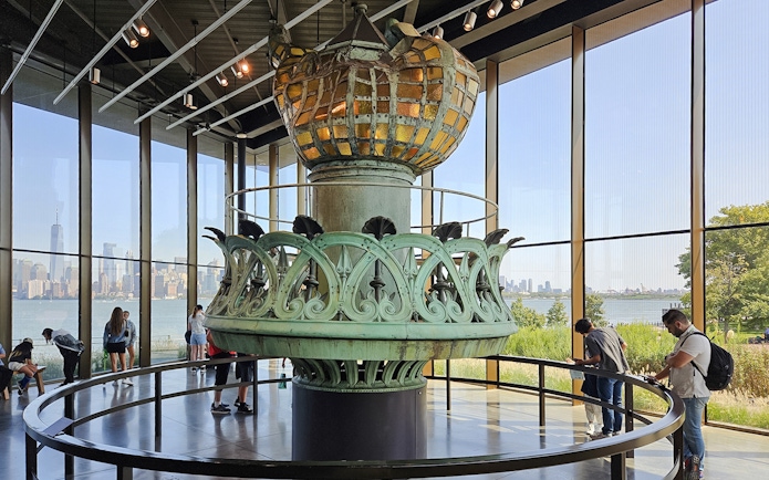 Original torch and crown spikes from the Statue of Liberty displayed indoors with city skyline view.