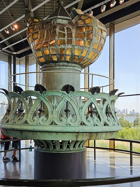 Original torch and crown spikes from the Statue of Liberty displayed indoors with city skyline view.