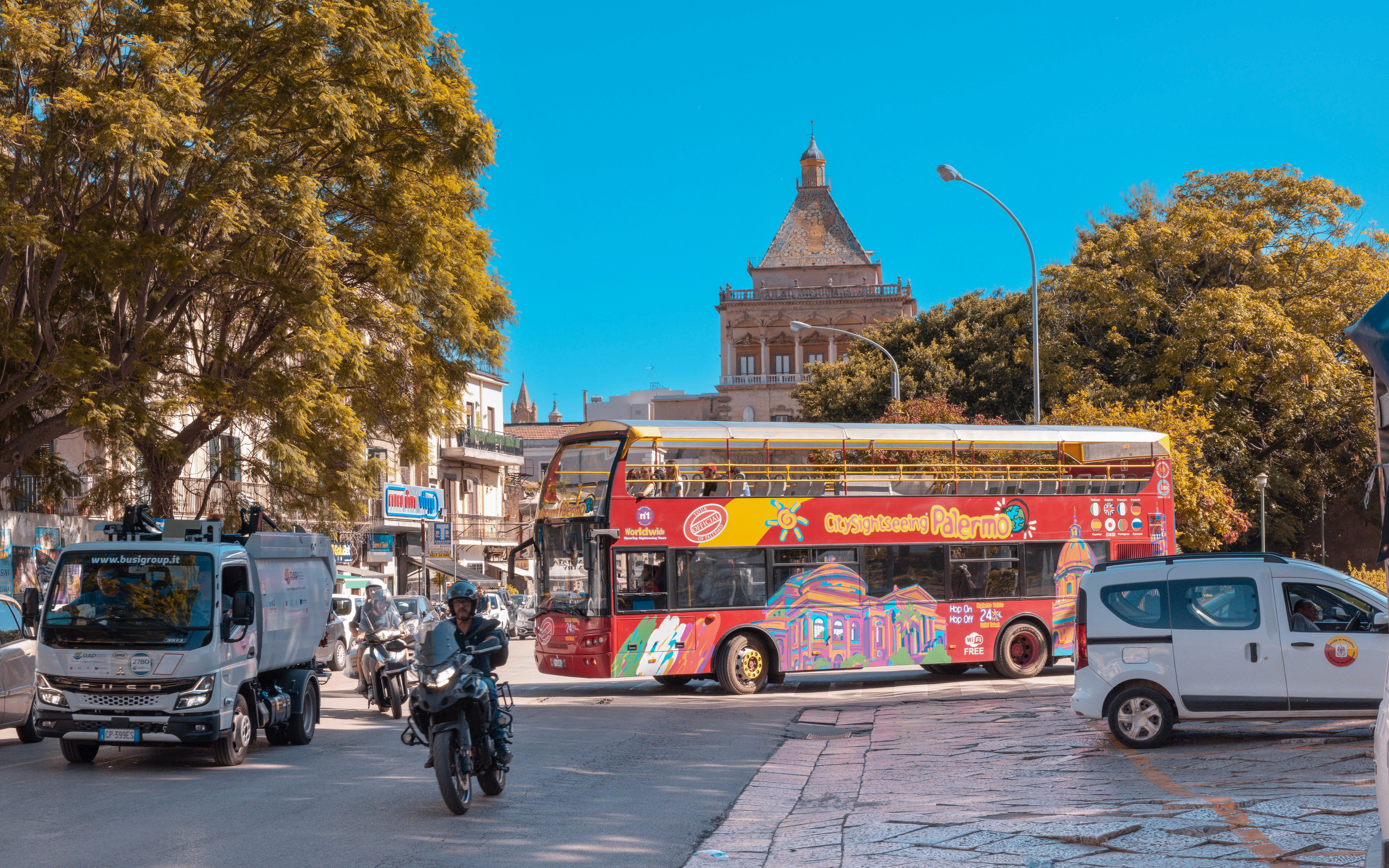 City Sightseeing bus in Palermo near historic building and trees.