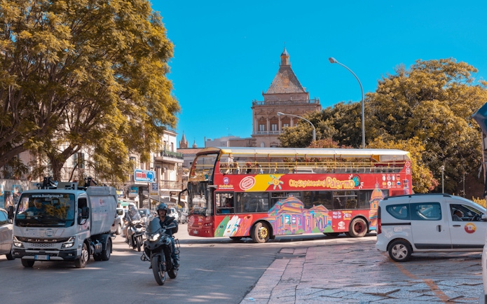 City Sightseeing bus in Palermo near historic building and trees.