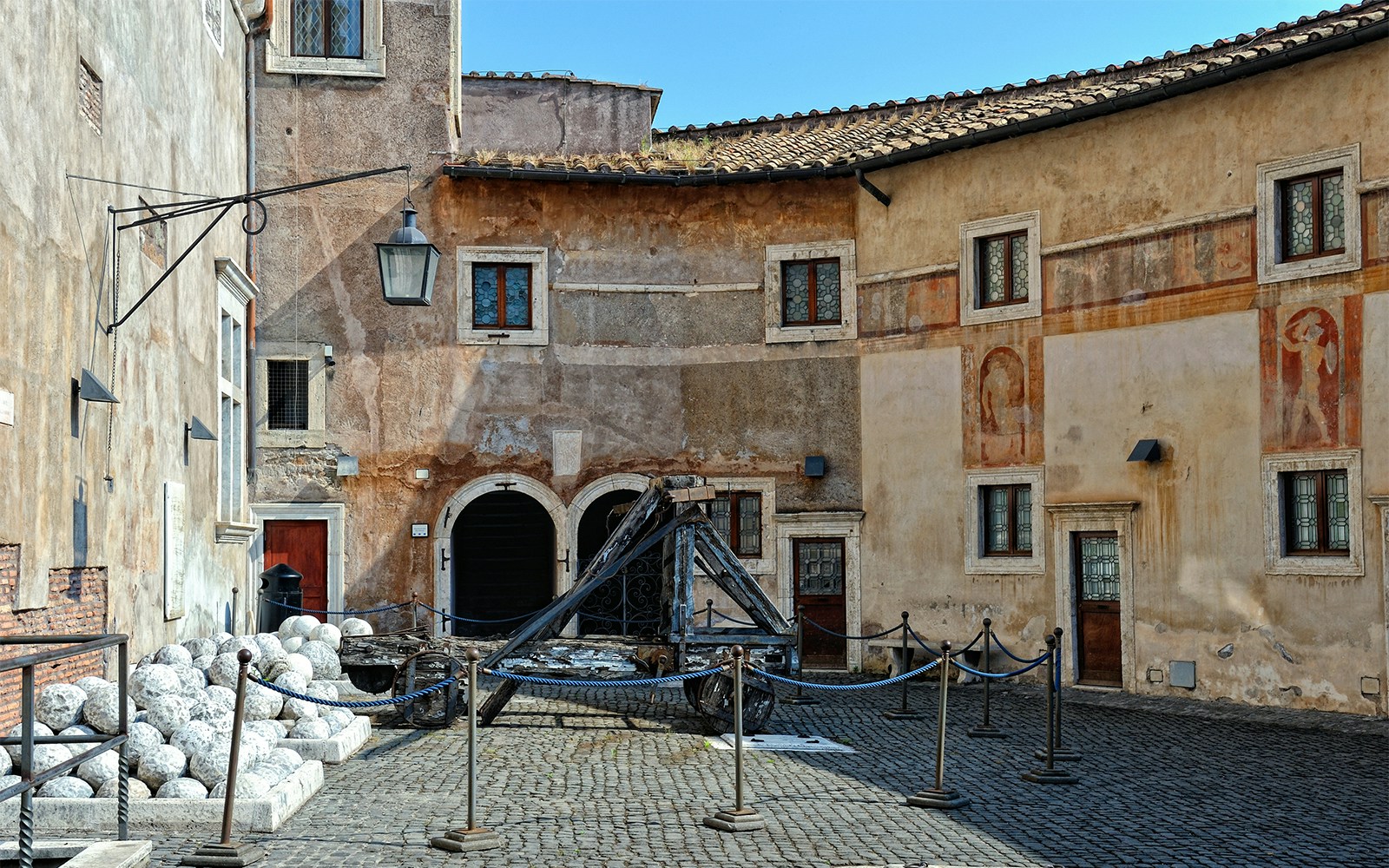 Courtyard of Castel Sant'Angelo in Rome with ancient catapult and stone cannonballs.