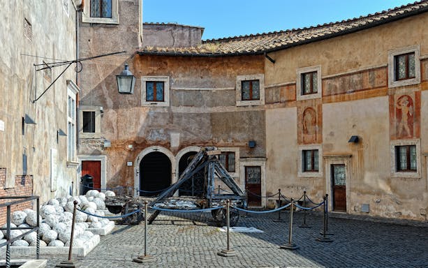 Courtyard of Castel Sant'Angelo in Rome with ancient catapult and stone cannonballs.